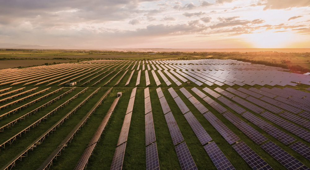 Luftaufnahme eines großen Solarparks in Brandenburg mit zahlreichen Solarmodulen in Reihen bei Sonnenuntergang